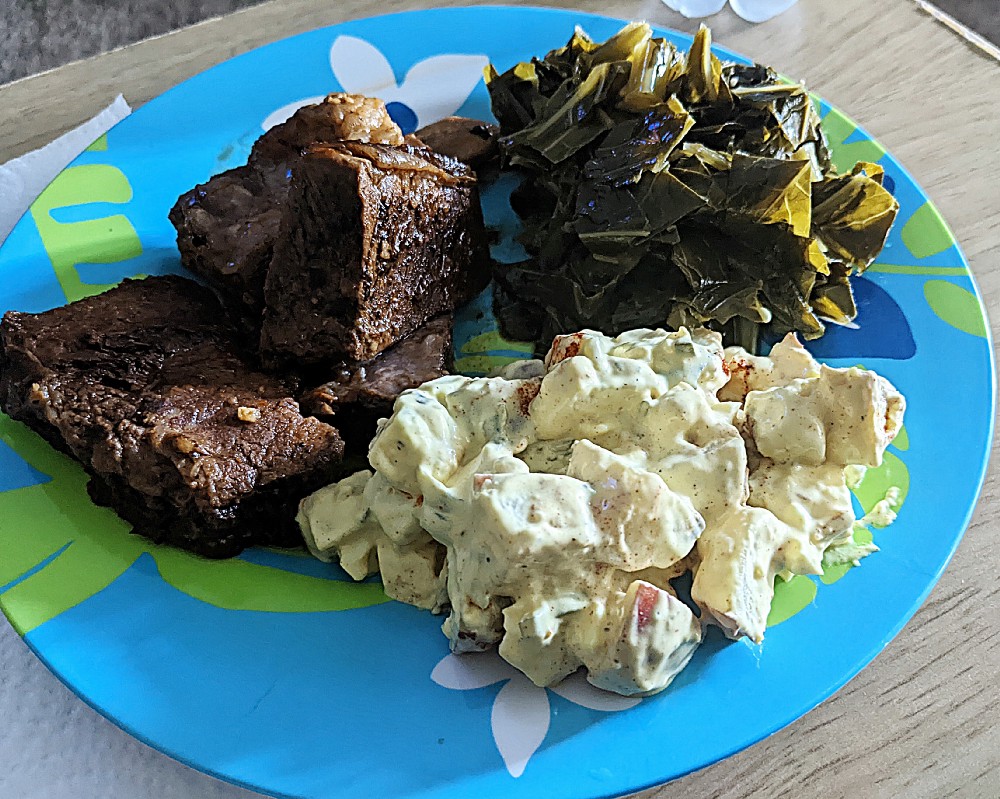 A photo of a home-cooked meal; bbq beef ribs, potato salad, and collard greens.