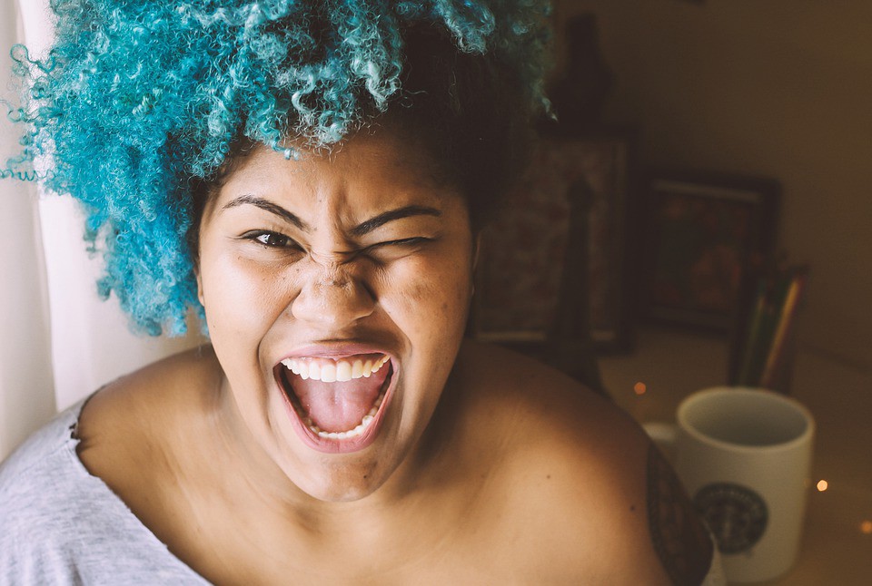 A photo of an excited, beautiful woman of color with blue hair.